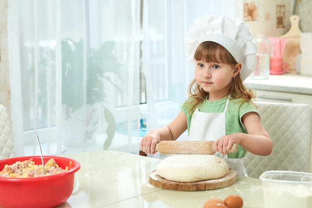 Het leuke meisje ontwikkelt deeg met een deegrol in keuken. ze is assistent.