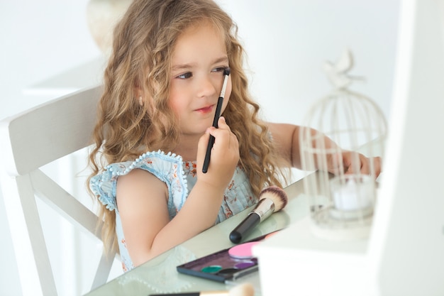 Het leuke meisje van toepassing zijn maakt omhoog het onderzoeken van spiegel. Weinig fashionistameisje die met haar moeder` s schoonheidsmiddelen spelen. Schattig kind binnenshuis