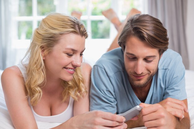 Foto het leuke paar ontspannen op bed die smartphone samen bekijken