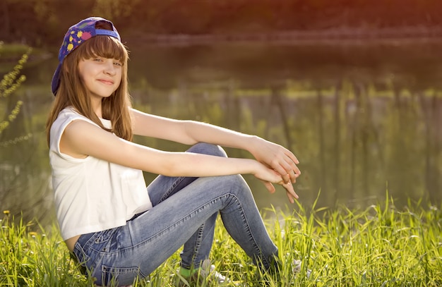 Foto het leuke tienermeisje zit op een gras dichtbij meer