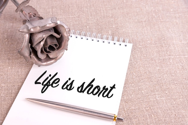 Het leven is kort, de tekst is geschreven in een notitieboek dat op een linnen linnen en een ijzeren rozenbloem ligt.