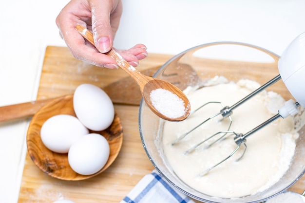 Het maken van deeg voor brood of zelfgemaakt gebak. ingrediënten op tafel. vrouwelijke handen houden een mixer vast voor het mengen van deeg