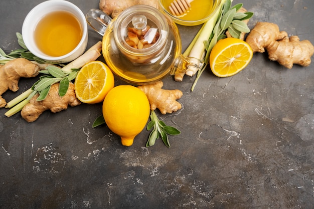 Het maken van gezonde antioxidant en ontstekingsremmende gemberthee met verse gember, citroengras, salie, honing en citroen op donkere achtergrond met kopie ruimte.