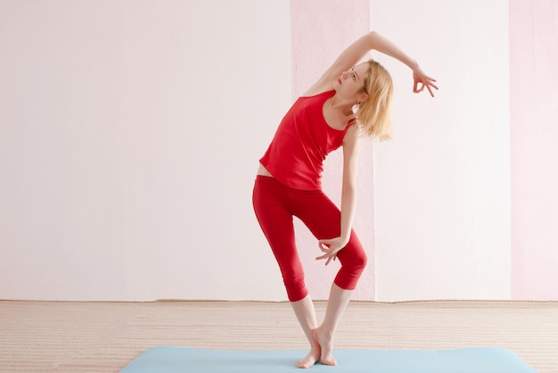 Het meisje beoefent yoga in rode sportkleding in de studio. Stelt in yoga. Kopieer ruimte