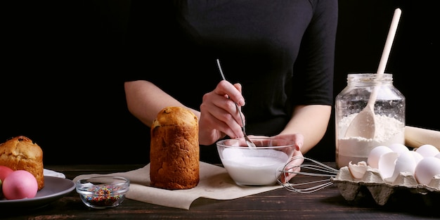 Het meisje bereidt Pasen bakken, smeert de cake met ijsvorming en bestrooit met gekleurd poeder