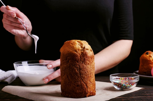 Het meisje bereidt Pasen bakken, smeert de cake met ijsvorming en bestrooit met gekleurd poeder