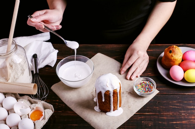 Het meisje bereidt Pasen bakken, smeert de cake met ijsvorming en bestrooit met gekleurd poeder