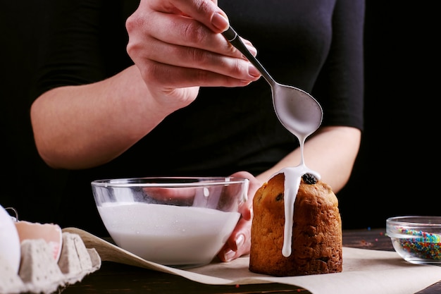 Het meisje bereidt Pasen bakken, smeert de cake met ijsvorming en bestrooit met gekleurd poeder