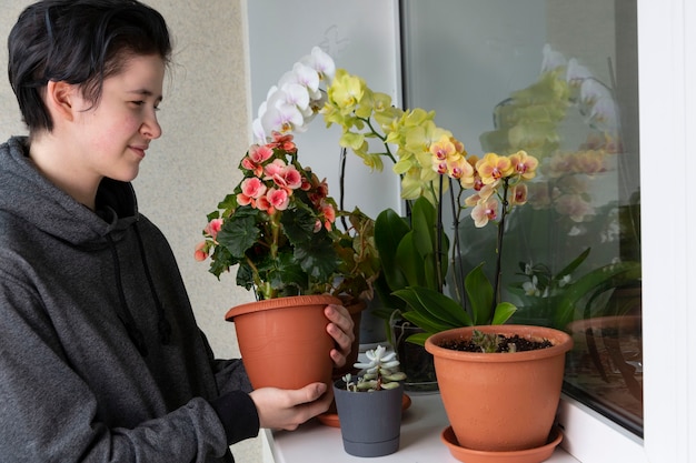 Het meisje bewondert de bloeiende planten op de vensterbank Huisplanten groene huis levensstijl