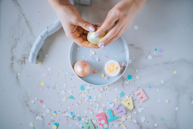 Het meisje breekt gouden paaseieren op marmeren achtergrond, confettien, fonkelingen, linten.