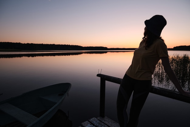 Het meisje dat bij zonsondergang op de pier bij het water staat