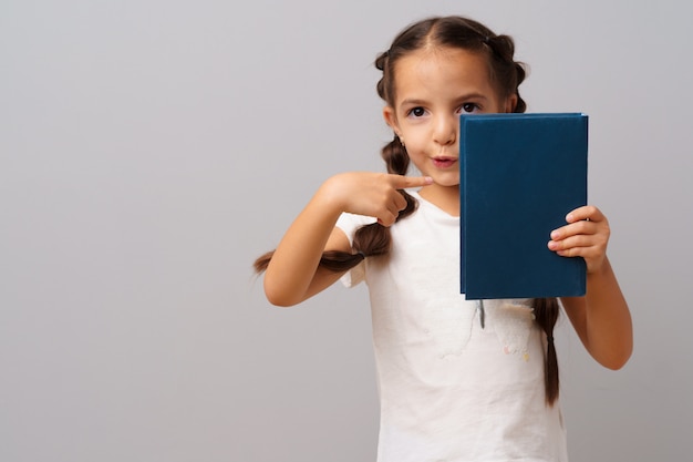 Het meisje dat een boek in haar houdt overhandigt een grijze achtergrond