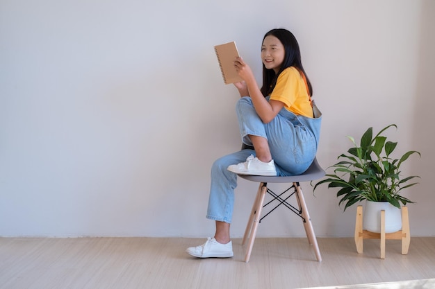 Het meisje dat op een stoel zit en een boek vasthoudt in een minimale kamer