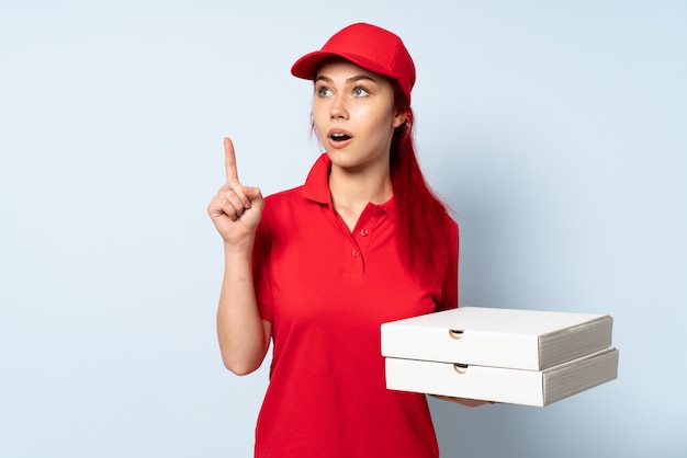 Het meisje dat van de pizzakoerier een pizza over geïsoleerde muur houdt denkend een idee dat de vinger benadrukt