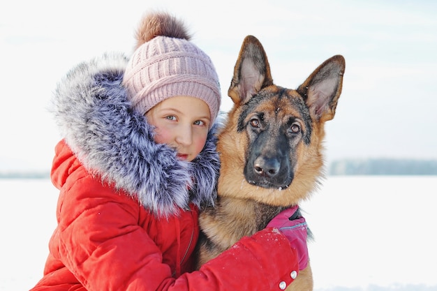 Het meisje dat zijn geliefde puppy knuffelt in het met sneeuw bedekte park. Duitse herdershond en kind op witte sneeuw in de winterdag. Zorg voor huisdieren. Levensstijl.