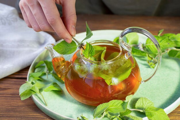 Het meisje doet muntblaadjes in een glazen theepot met groene thee Gezonde voeding antioxidanten