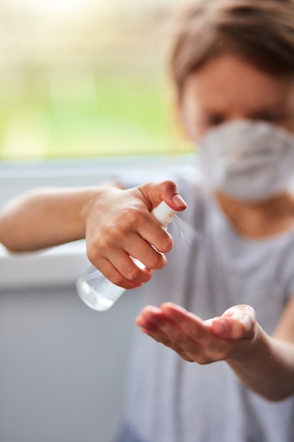 Het meisje draagt een hygiënisch masker en drukt op alcoholspray om te beschermen, te ontsmetten.