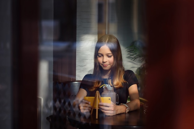 Het meisje drinkt koffie en let op video op mobiele telefoon