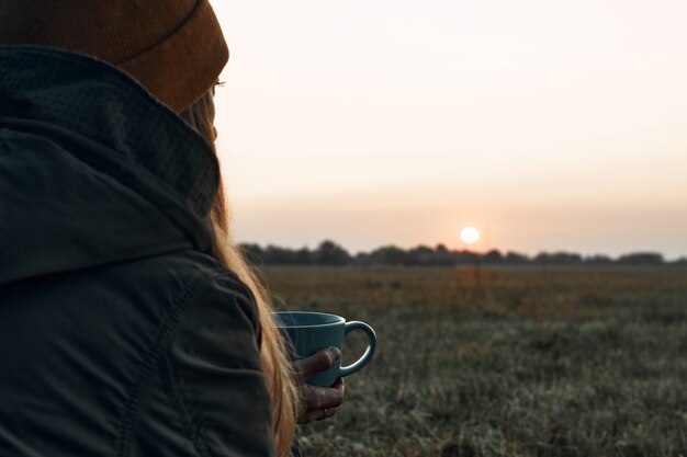 Het meisje drinkt uit een beker en kijkt naar de koude dageraad. Reizen.