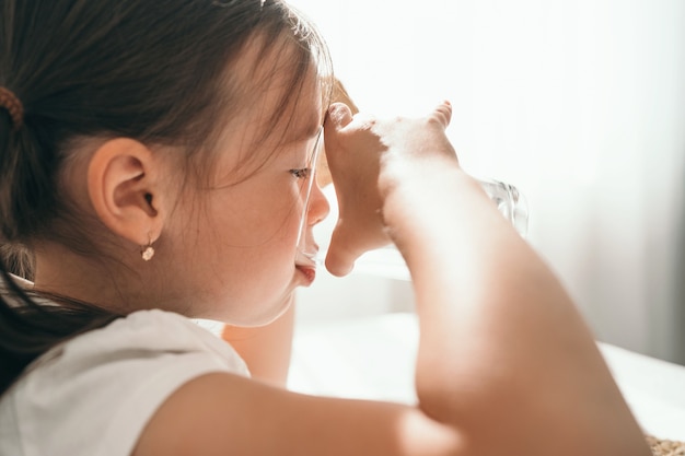 Het meisje drinkt water uit een glazen glas. Een klein meisje lest haar dorst