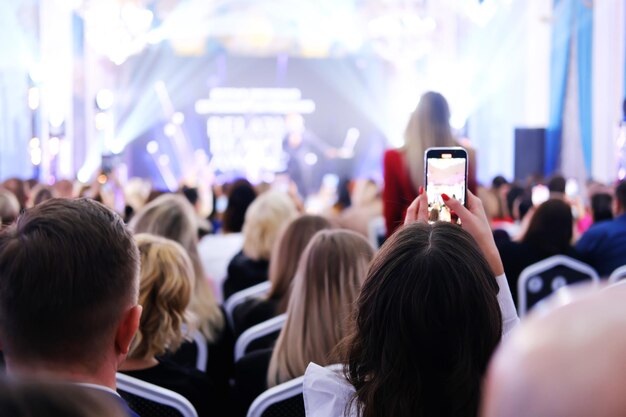 Het meisje fotografeert het evenement aan de telefoon Gasten in avondkleding zitten in een verlichte lobby en kijken naar het podium