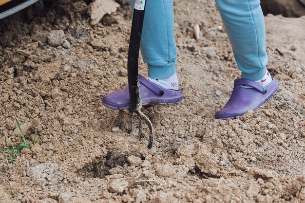 Het meisje graaft de grond met een hooivork in de tuin om een gat te maken voor het planten van een plant
