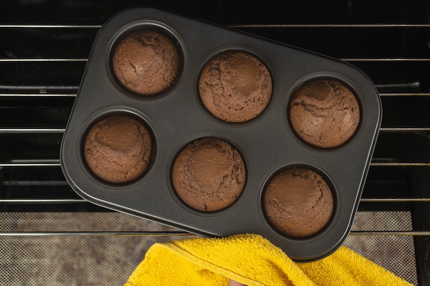 Foto het meisje haalt een bakplaat met chocolademuffins uit de oven.