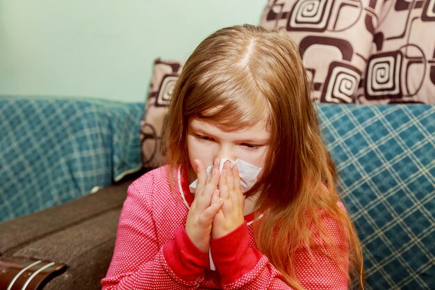 Het meisje heeft een loopneus en blaast haar neus in een papieren zakdoek