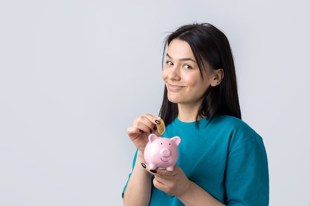 Het meisje heeft een roze spaarvarken en een munt in haar handen. Het concept van rijkdom en accumulatie.