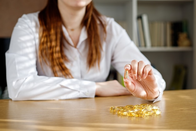 Het meisje heeft een visoliecapsule in haar hand. Omega-3 capsules op tafel en in de hand van de dokter.