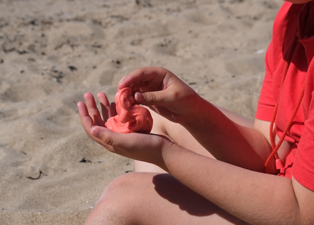 Het meisje heeft rood slijm in haar handen. Het meisje is altijd enthousiast over het spelen met slijm, zelfs op het strand kalmeert het spelen met slijm haar.