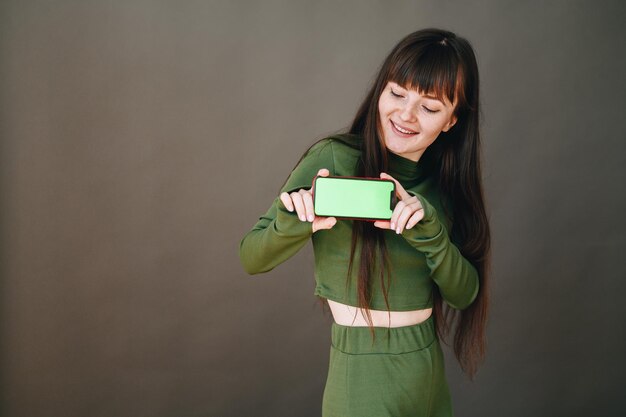 Het meisje houdt de telefoon met beide handen vast met een groen scherm naar voren en kijkt naar de telefoon