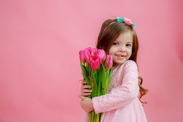 Het meisje houdt een boeket tulpen op een roze achtergrond