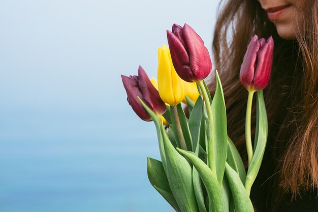 Het meisje houdt een boeket van heldere tulpen op de achtergrond van blauwe overzees