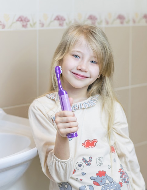 Het meisje houdt een elektrische tandenborstel in haar hand.