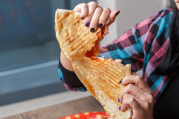 Het meisje houdt een quesadilla in haar handen, ligt op een bord, bijt en braakt, lichte en donkere achtergrond