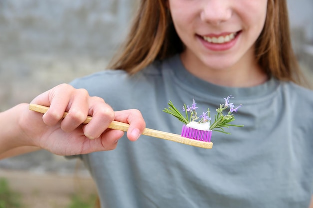 Het meisje houdt een tandenborstel met gekruide tandpasta met rozemarijn in haar hand selectieve focus op tandenborstel en rozemarijn