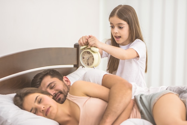 Het meisje houdt een wekker bij de ouders in bed