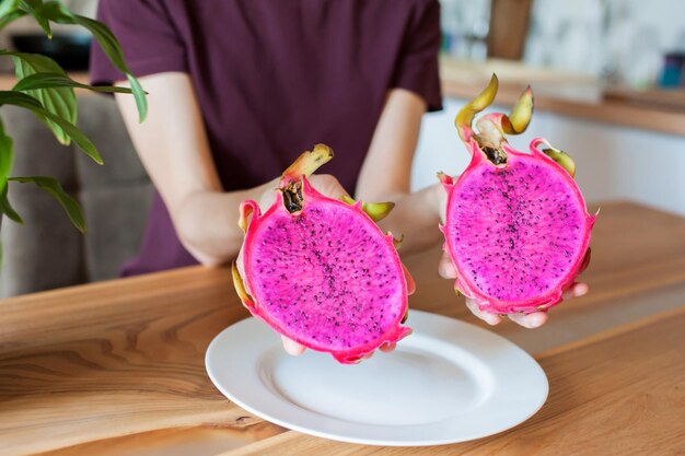 Foto het meisje houdt in haar handen een gesneden draak fruit pitahaya thuis in de keuken close-up zachte focus