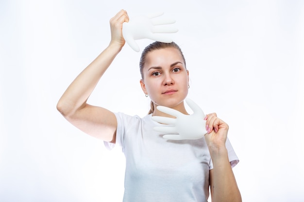 Het meisje houdt witte medische handschoenen in haar handen. bescherming tegen ziektekiemen en het virus. ze is in een wit t-shirt op een witte achtergrond.