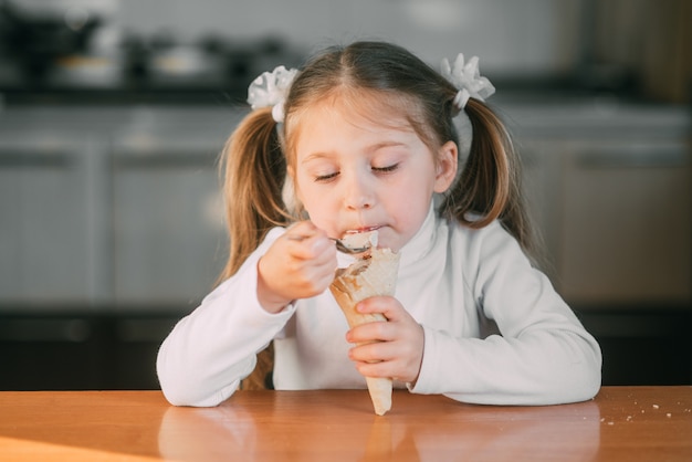 Het meisje in de keuken eet het ijshoorntje met een lepel het licht van de dag heel lief