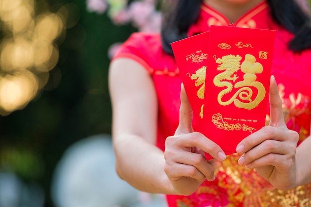 Foto het meisje in de rode jurk van chinese afkomst is blij met de rode envelop met de dollar.