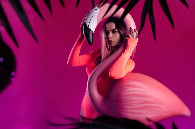 Het meisje in een felgekleurde bodysuit poseert met een groot flamingo-beeldje