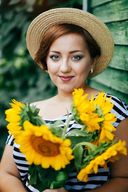 Het meisje in een hoed met een boeket zonnebloemen poseert