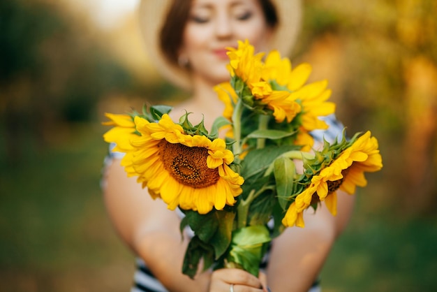 Het meisje in een hoed met een boeket zonnebloemen poseert