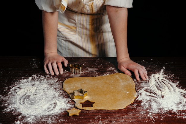 Het meisje in een schort snijdt deegvormige koekjes in de vorm van sterren op een houten tafel