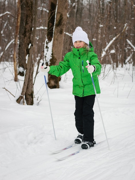 Het meisje in het groene pak loopt langzaam door het bos op ski's