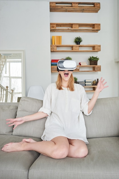 Het meisje in het wit zittend op een grijze bank in een virtual reality-helm