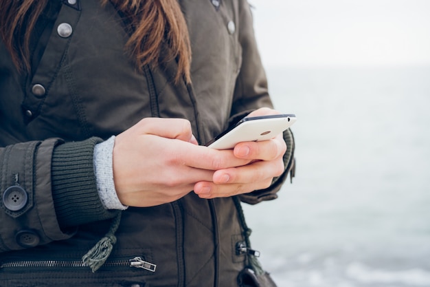 Het meisje in jasje gebruikt een smartphone terwijl het lopen langs het strand