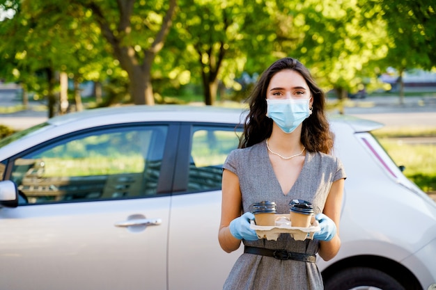 Het meisje in medisch masker en handschoenen houdt dienblad met wegwerpkoffiekopjes